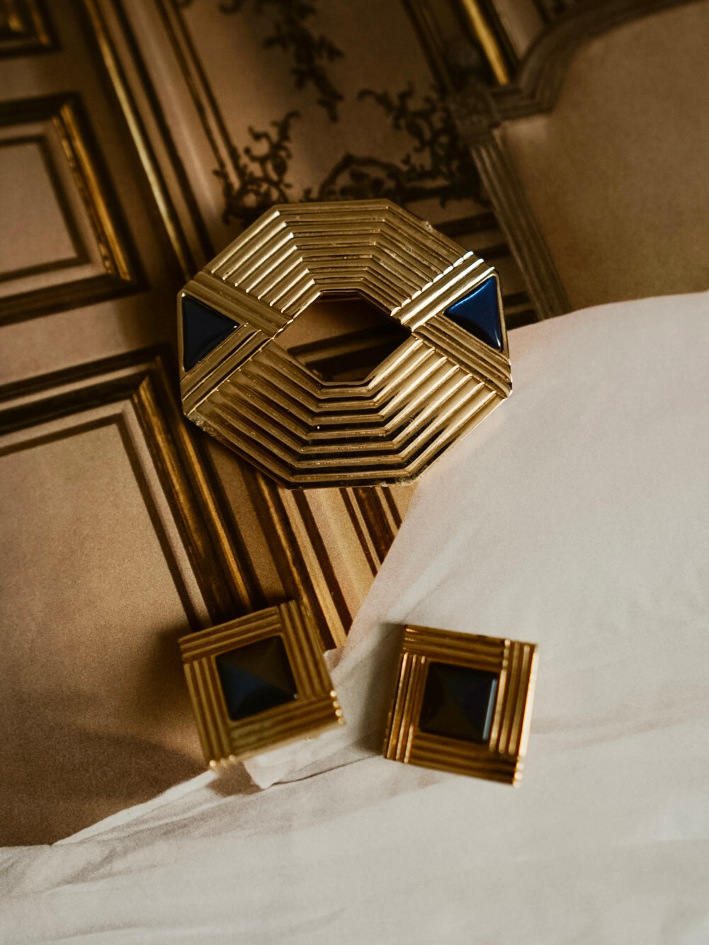 Gold geometric jewelry set featuring a large octagonal ring with blue triangular accents and two matching square earrings.