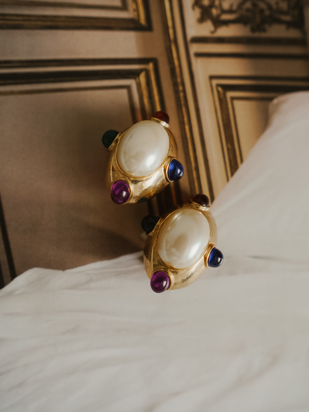 A pair of gold statement rings with large oval white pearl-like centers and small colorful gemstone accents.